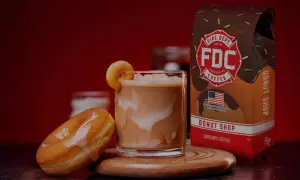 Ein cremiger iced americano mit einem Donut-Garnitur, daneben ein Donut und eine Packung Fire Dept. Coffee.