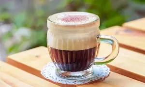 Ein Glas mit cremigem Kaffee mit Ei, bestäubt mit Kakao, steht auf einem Holztisch.