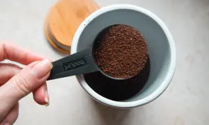 Eine Hand hält einen Löffel mit frisch gemahlenem Kaffeepulver, bereit, es in einen Behälter zu geben. Die Frage ist: wie viel Kaffeepulver für den perfekten Morgen?
