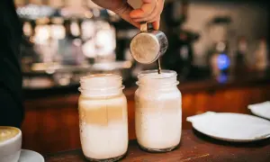 Zwei Latte Macchiato in Gläsern, ein Barista gießt Espresso ein. Kalorienbewusst genießen?