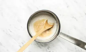 Ein Holzlöffel rührt in einem Topf mit cremiger Hafermilch, die für einen köstlichen Hafermilch-Latte vorbereitet wird.