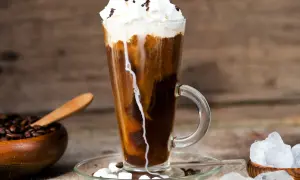 Ein erfrischender iced espresso mit Sahne, Marshmallows und Schokostreuseln, daneben Kaffeebohnen und Eiswürfel.