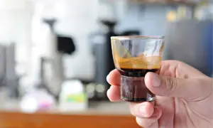 Eine Hand hält ein kleines Glas mit einem dunklen, cremigen Ristretto. Die Zubereitung ist perfekt, die Crema glänzt.