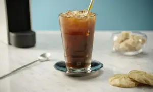Erfrischender Nespresso Iced Coffee mit Eiswürfeln und einem bunten Strohhalm, daneben Kekse und Zuckerwürfel.