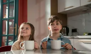 Zwei Kinder mit Tassen, die sich fragen, ab welchem Alter man Kaffee trinken darf. Der Junge leckt sich die Lippen.