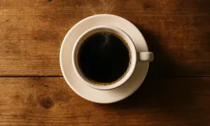 Eine Tasse dampfender schwarzer Kaffee auf einem Holztisch. Schwarzer Kaffee hat kaum Kalorien, perfekt für eine bewusste Ernährung.