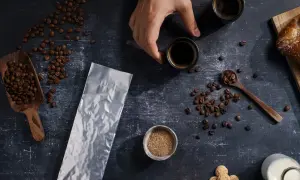 Kaffeebohnen, eine leere Vakuumverpackung für lange Haltbarkeit, Zucker und zwei Espressotassen.