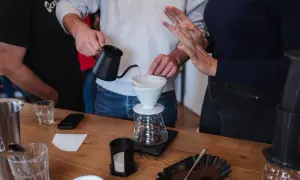 Hände bereiten Kaffee zu, die **Koffeinwirkung** wird bald spürbar sein. Wasser fließt in einen Filter über einer Karaffe.