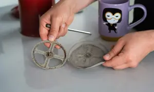 Hände zerlegen eine schmutzige French Press, um sie zu reinigen. Der Siebträger und das Sieb sind mit Kaffeesatz bedeckt.