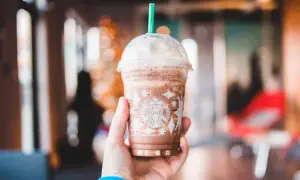 Eine Hand hält einen Schokoladen-Frappuccino von Starbucks, der mit Schlagsahne und einem grünen Strohhalm gekrönt ist. Perfekt für heiße Tage, diese Starbucks Rezepte Frappuccino sind ein Genuss.