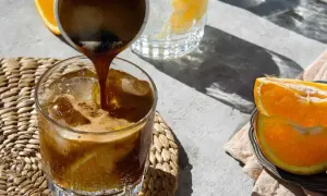 Espresso wird in ein Glas mit Eis und Orangenscheiben gegossen. Ein erfrischender Espresso Tonic für heiße Tage.