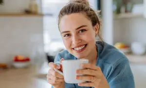 Lächelnde Frau hält eine Tasse Kaffee. Sie genießt den Moment, vielleicht trinkt sie alten Kaffee, um den Tag zu beginnen.