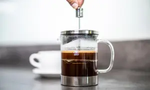 Eine Hand drückt den Stempel einer French Press herunter. So funktioniert eine French Press: Kaffee und heißes Wasser ziehen lassen, dann den Kaffeesatz abpressen.
