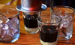 Zwei Gläser mit süßer Kondensmilch und starkem Kaffee, bereit für Eiswürfel. Ein vietnamesischer Eiskaffee zum Genießen.