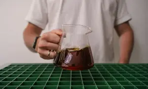 Person hält ein Glasgefäß mit frisch gebrühtem Kaffee, der gerade extrahiert wurde.