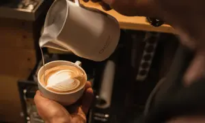 Barista kreiert ein Herz-Latte-Art-Muster, indem er Milchschaum in Kaffee gießt.