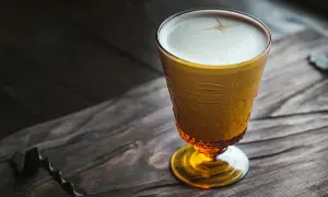 Ein goldener Becher mit cremigem Schaum, der an einen russischen Kaffee erinnert, steht auf einem rustikalen Holztisch.