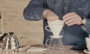 Mann bereitet sich auf das Kaffee filtern vor, indem er den Papierfilter in den Trichter legt.