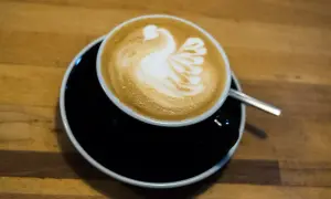 Kaffee mit einem Schwan aus Milchschaum zubereitet, serviert auf einem schwarzen Unterteller.