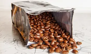 Ein offener Beutel mit gerösteten Kaffeebohnen, die auf eine gemusterte Oberfläche fallen. Die Frage, wie lange sind kaffeebohnen haltbar, beschäftigt jeden Kaffeeliebhaber.