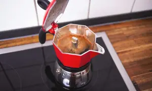 Roter Espressokocher auf dem Herd, der frischen Kaffee zubereitet. Der Duft von heißem Kaffee liegt in der Luft.