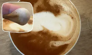 Ein Finger berührt den Schaum eines Kaffees mit Mandelmilch. Der cremige Schaum bildet ein Herzmuster.