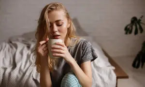 Junge Frau sitzt im Bett, hält eine Tasse und denkt nach. Ihr Kaffee schmeckt nicht mehr.