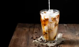 Milch wird in ein Glas mit Eis und Kaffee gegossen. Ein erfrischender Eiskaffee auf einem Holztisch.