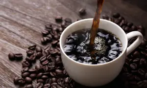 Heißer schwarzer Kaffee wird in eine weiße Tasse gegossen, umgeben von gerösteten Kaffeebohnen. Ein gesunder Start in den Tag.