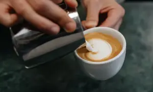 Barista gießt Milch in Kaffee, um ein Latte Art Herz zu kreieren.