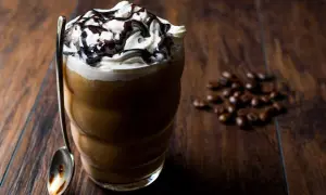 Eisgekühlter Kaffee mit Sahne und Schokoladensauce, ein köstliches Frappuccino Rezept. Daneben liegen geröstete Kaffeebohnen.