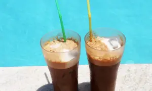 Zwei erfrischende Cafe Frappe mit Eis und Schaum stehen am Poolrand.