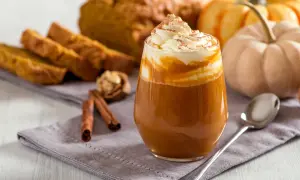Ein cremiger Pumpkin Spice Latte mit Sahne und Zimt, daneben Kürbisbrot und Zimtstangen. Ein Genuss, der die pumpkin spice latte kalorien vergessen lässt.