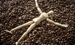 Holzfigur liegt auf einem Berg gerösteter Kaffeebohnen. Sieht aus, als würde sie die Kaffeebohnen kauen.