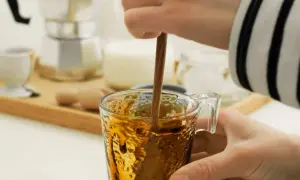Eine Hand rührt mit einem Holzstäbchen in einem Glas Kaffee. Perfekt für die Kaffeesirup Verwendung für süße Kaffeekreationen.