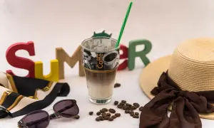 Ein erfrischender Vanilla Iced Coffee steht bereit für einen sonnigen Sommertag, umgeben von bunten Buchstaben, einer Sonnenbrille und einem Strohhut.