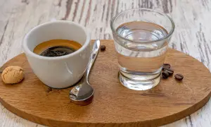 Ein Espresso mit einem Glas Wasser, einem Keks und Kaffeebohnen. Das Wasser ist wichtig, um den Gaumen zu reinigen und den vollen Geschmack des Espressos zu genießen.