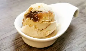 Cremiges Eis mit Karamellsauce, das an einen iced macchiato erinnert, in einer weißen Schale auf Holztisch.