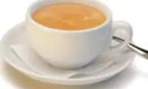 Eine Tasse mit cremigem, braunem Kaffee steht auf einer Untertasse. Ein kleiner Löffel liegt daneben.
