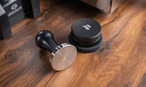 Ein Tamper ist ein Werkzeug zum Verdichten von Kaffeepulver im Siebträger. Hier liegt ein schicker Tamper neben einem Kaffee-Dosierring.