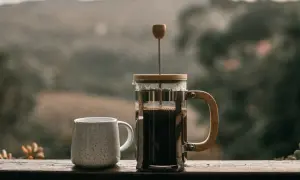 Eine French Press, bereit für den perfekten Kaffee. Neben einer Tasse wartet sie auf den Genuss.