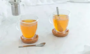 Zwei Tassen mit warmem Tee, ideal bei Halsschmerzen. Ein Teekännchen steht im Hintergrund.