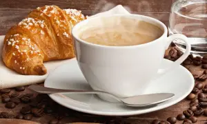 Dampfender Cappuccino mit Croissant und Kaffeebohnen. Ein Genuss, der die **Cappuccino Kalorien** wert ist.