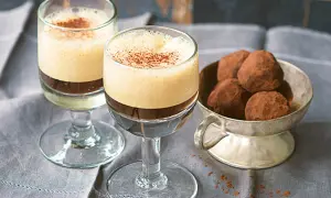 Zwei Gläser mit cremigem Caffe Shakerato, bestäubt mit Kakao. Daneben eine Schale mit Schokoladentrüffeln.