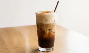 Ein erfrischender, geschüttelter Espresso mit cremiger Haube und Zimt bestreut, serviert in einem Glas mit Eiswürfeln und einem Metallstrohhalm.