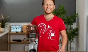 Mann in rotem T-Shirt mit Eichhörnchen-Aufdruck hält Kaffeemühle, bereit für perfekten Ristretto ml.