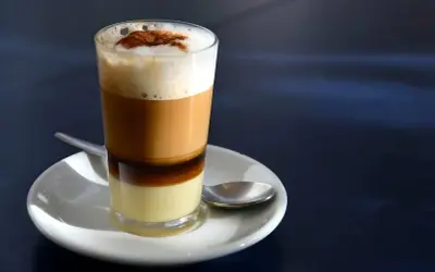 Ein geschichteter Kaffee mit Kondensmilch, Espresso und Milchschaum, bestreut mit Zimt. Ein süßer Genuss, wie ein flüssiger bonbon kaffee.