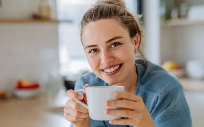 Lächelnde Frau hält eine Tasse Kaffee. Sie genießt den Moment, vielleicht trinkt sie alten Kaffee, um den Tag zu beginnen.