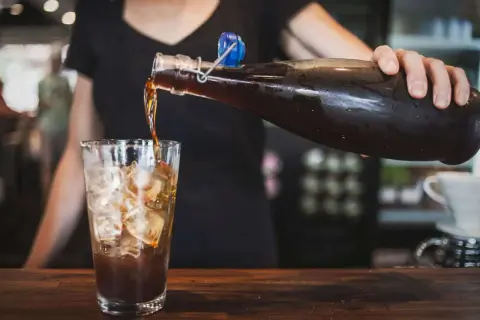 Eine Person gießt Cold Brew Kaffee mit Eis in ein Glas. Cold Brew ist ein Kaffee, der kalt extrahiert wird.