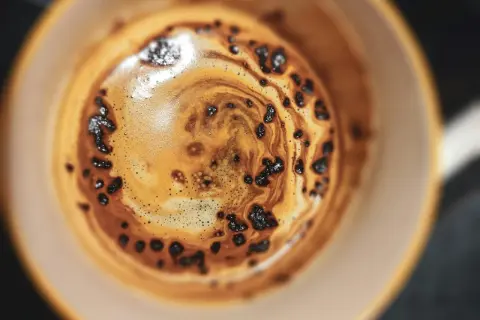 Nahaufnahme einer Tasse Kaffee mit Crema und Kaffeepulver, die an die Herstellung von Instantkaffee erinnert.